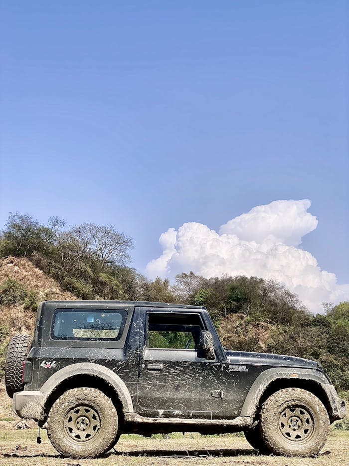 A rugged 4x4 jeep parked on muddy terrain under a clear blue sky with clouds.